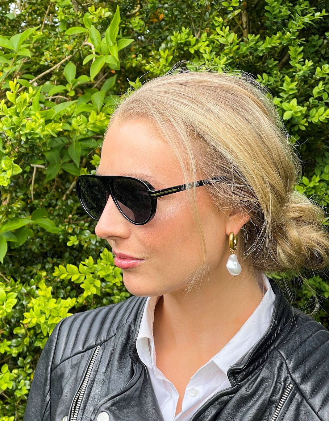 Modell med blondt hår iført PVD-belagte gulløredobber med barokkperler og Eagle-solbriller fra Mea Nani. Fotografert i naturlig sollys – perfekt sommerstil.