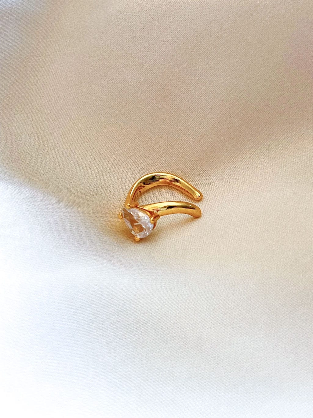 Earcuff i gull med glitrende stein på hvit bakgrunn