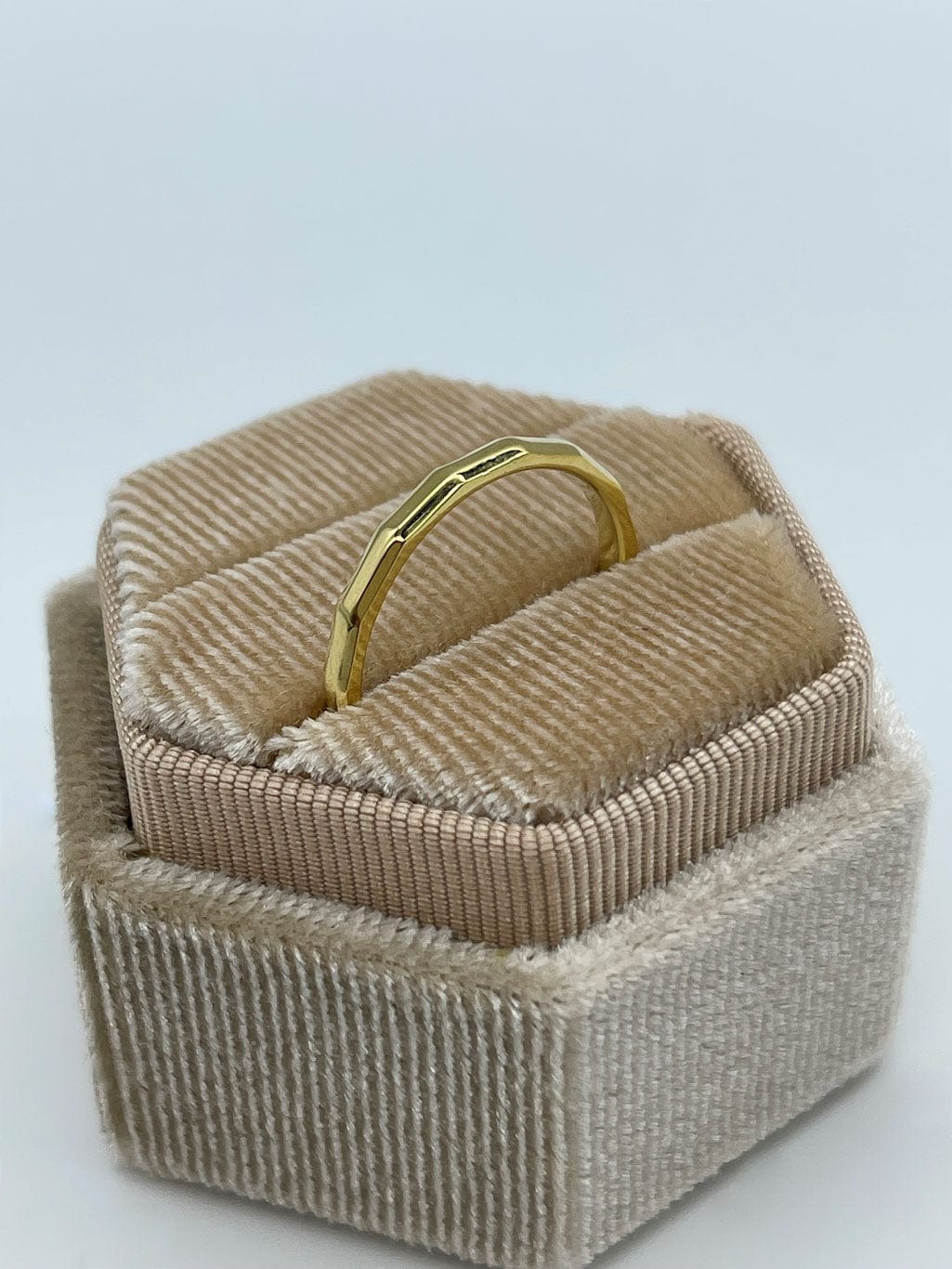 Gullbelagt kantete ring som står i en beige smykkeeske