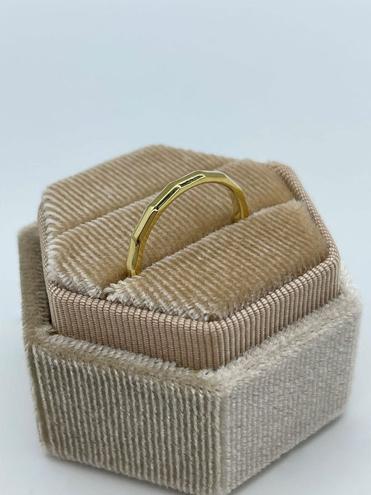 Gullbelagt kantete ring som står i en beige smykkeeske